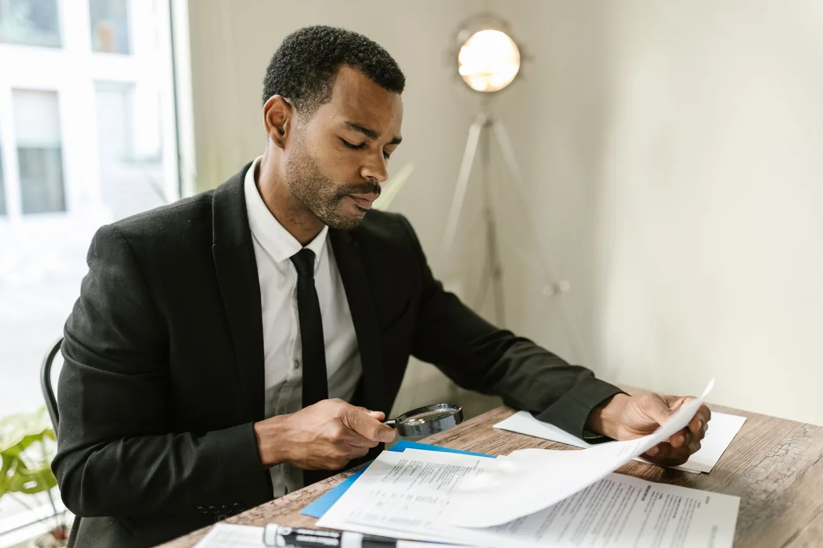 Professional man examines paperwork with magnifying glass at office desk, highlighting attention to detail.