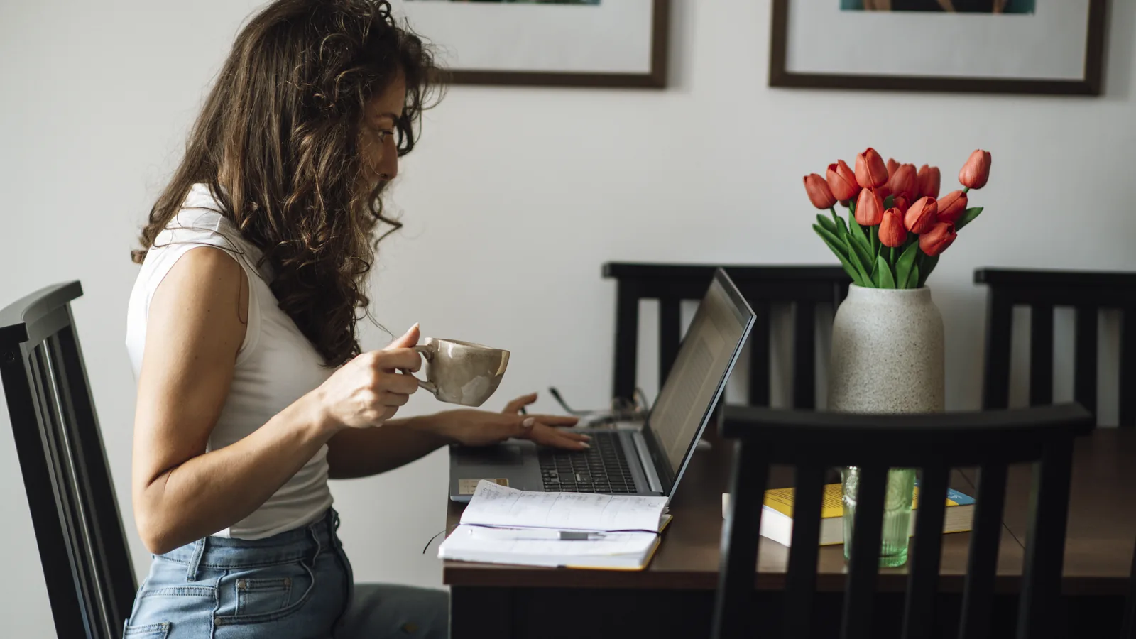 A person working on a laptop at a desk in a cozy home office while holding a cup of coffee